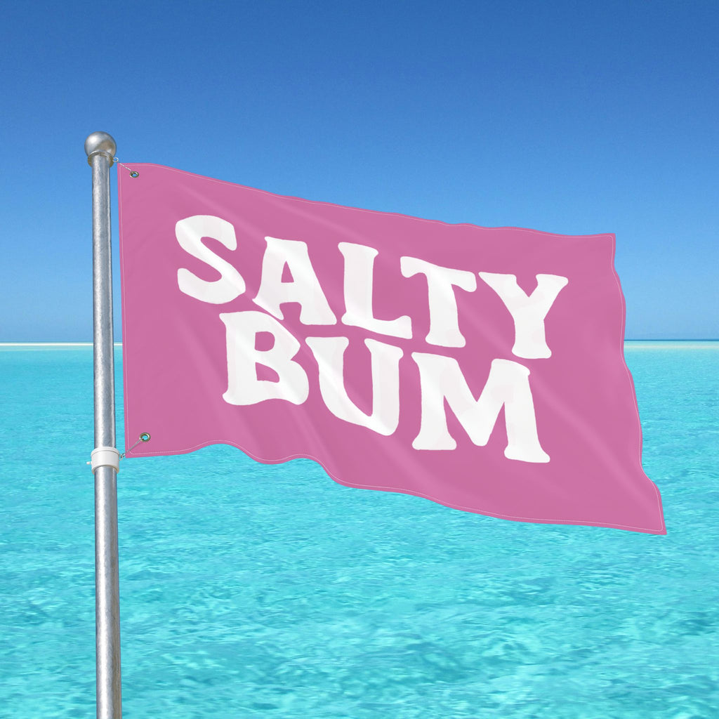 Pink flag with 'Salty Bum' text against a clear blue sky and ocean.