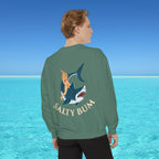 Person wearing a green sweatshirt with a shark and bikini graphic and 'Salty Bum' text, standing in front of a blue ocean.