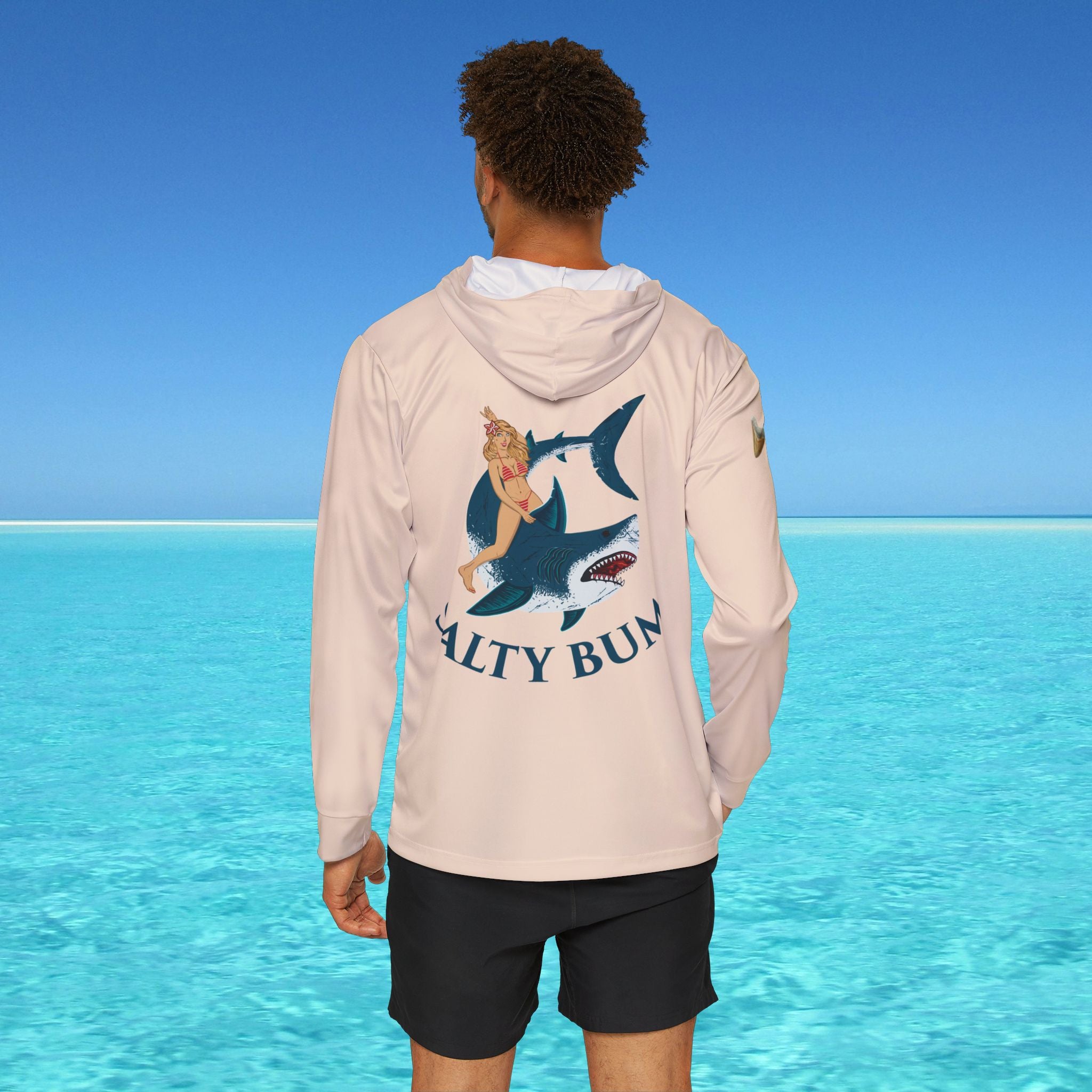 Person wearing a hoodie with a shark and mermaid design in front of clear blue water.