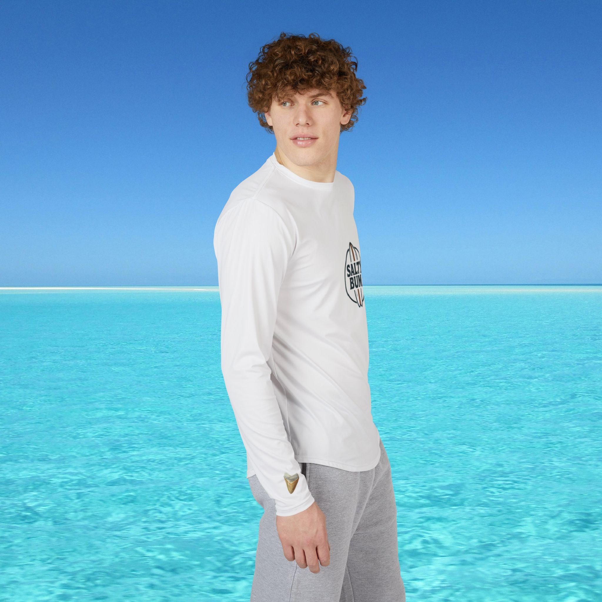 Person wearing a white long-sleeve shirt with a logo standing in front of clear blue water and sky.