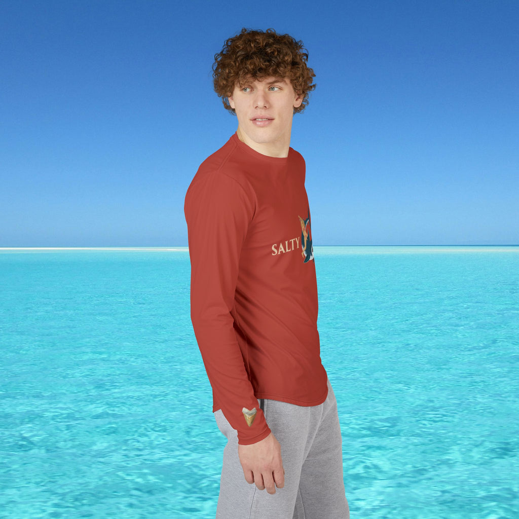 Person wearing a red long-sleeve shirt with 'Salt' branding by a clear blue ocean.