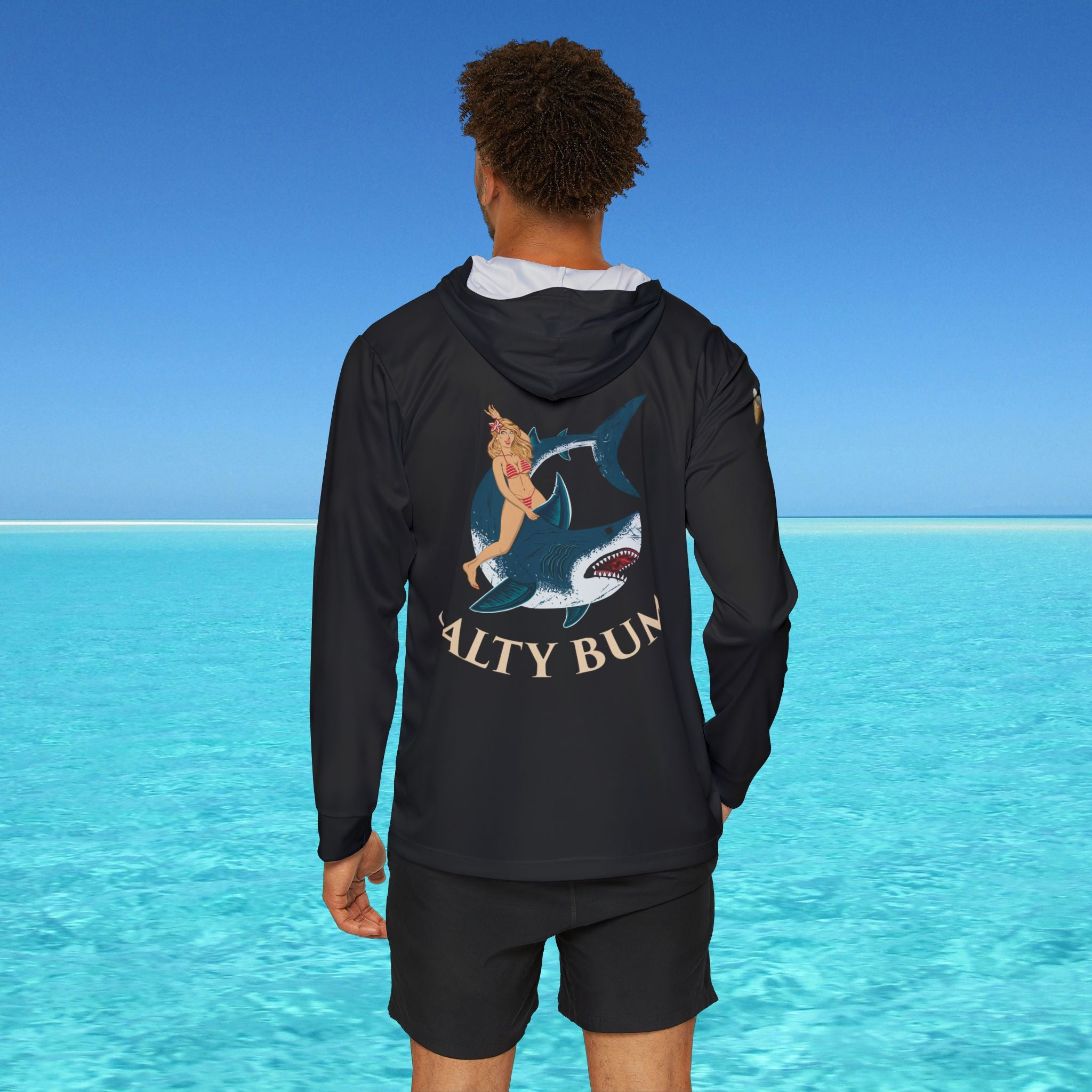 Person wearing a black hoodie with a shark graphic and 'Quality Bun' text, standing in front of clear blue water.