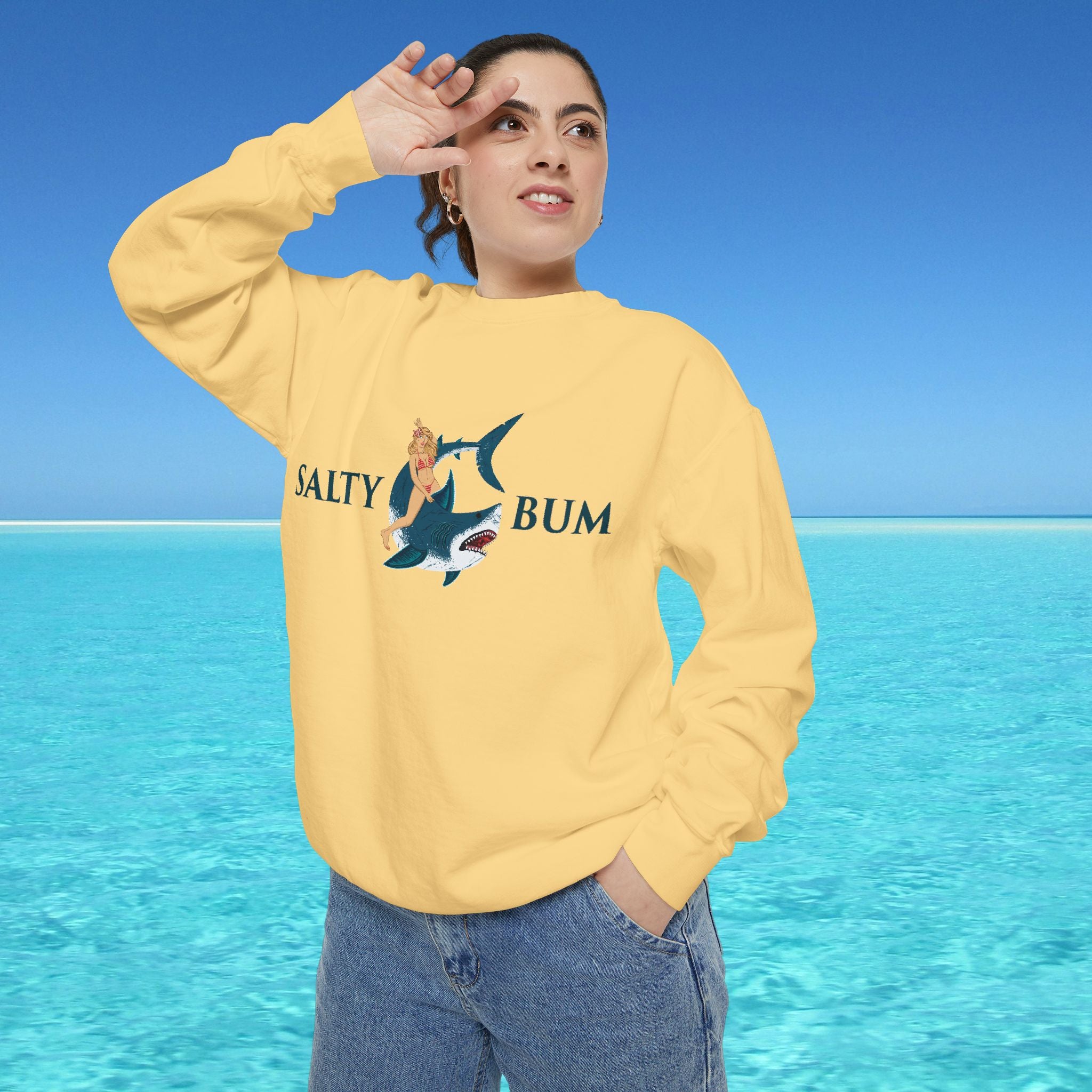 Person wearing a yellow sweatshirt with a shark graphic and text, standing in front of a blue ocean.