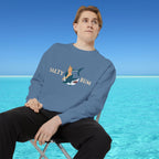 Person wearing a blue sweatshirt with a graphic design sitting on a chair by a blue ocean.