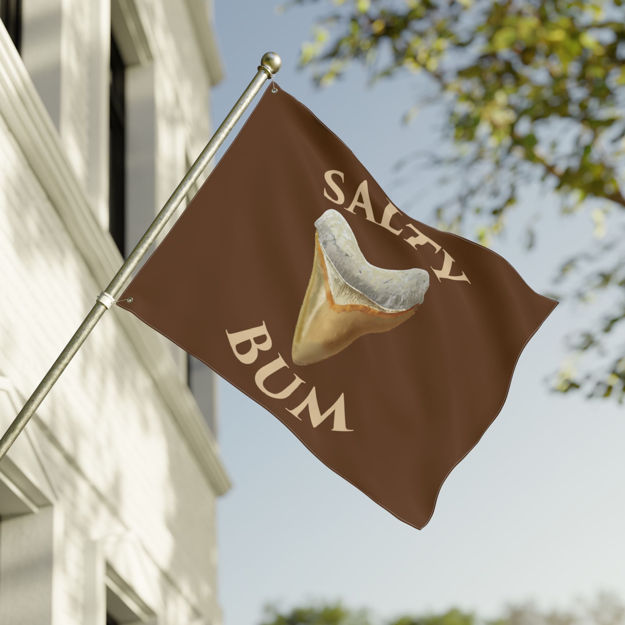 Flag with 'Salty Bum' design on a pole against a building and tree background
