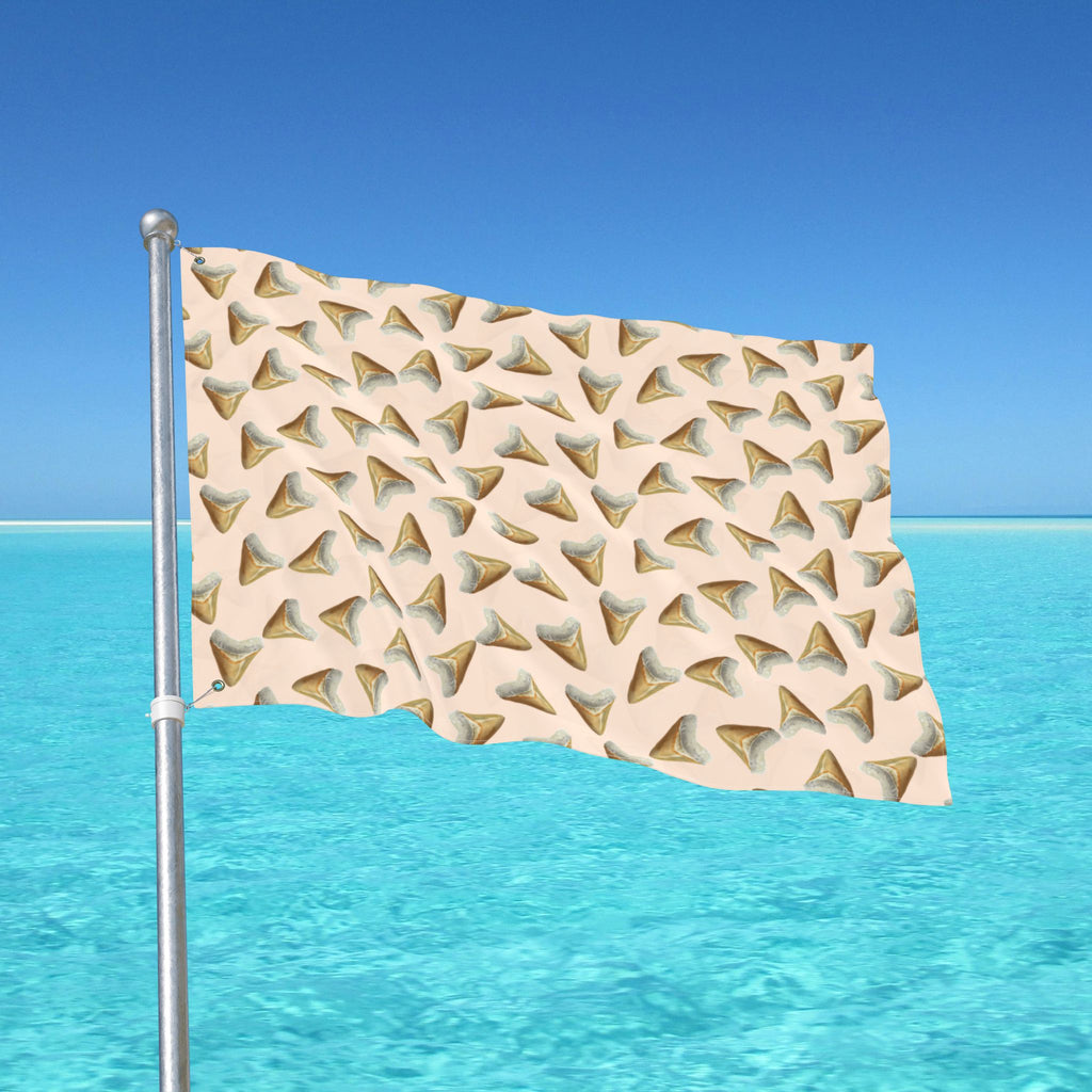Flag with shark tooth pattern waving in the wind against a clear blue sky and ocean.