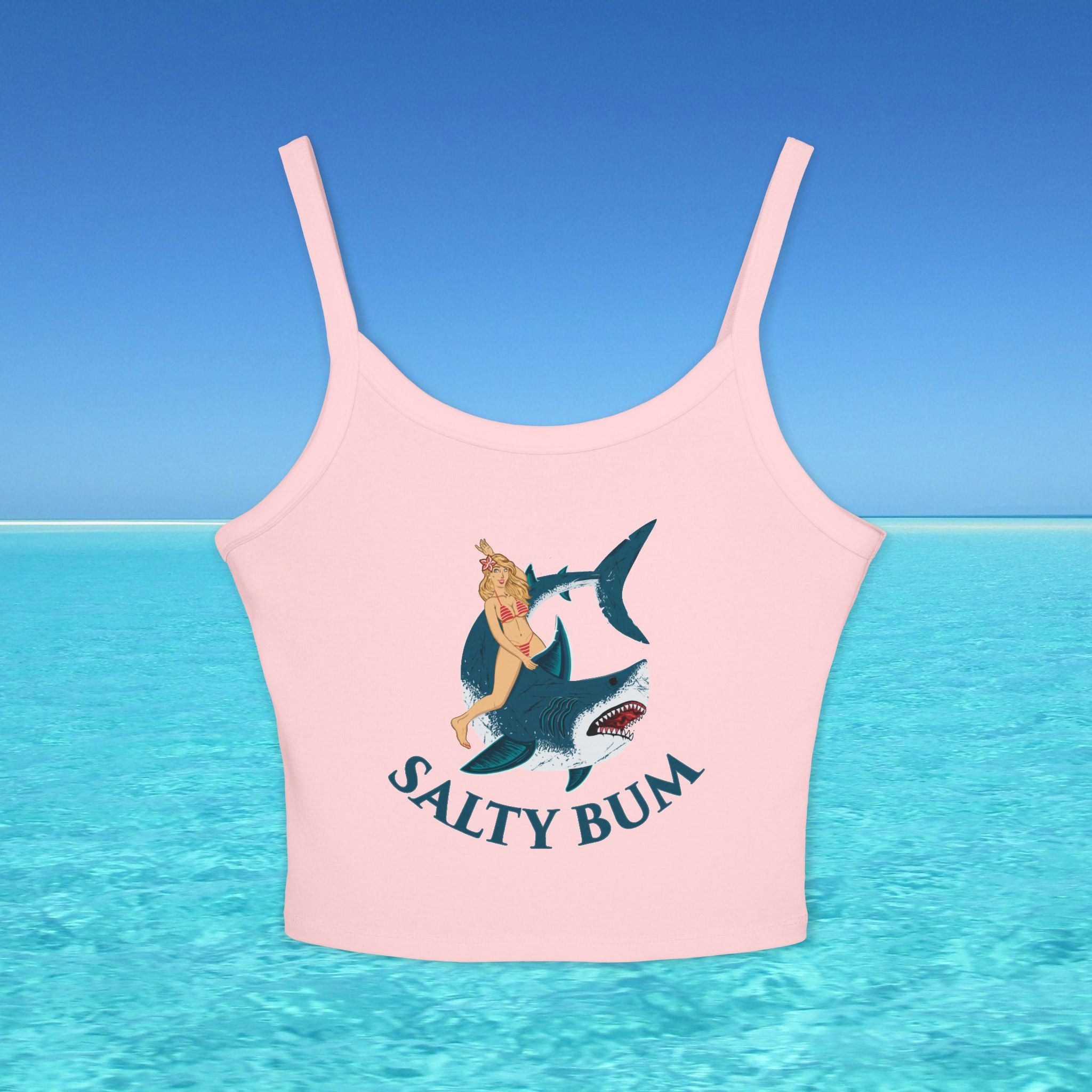 Pink crop top with a graphic of a woman on a shark and 'Salty Bum' text, set against a blue ocean and sky background.