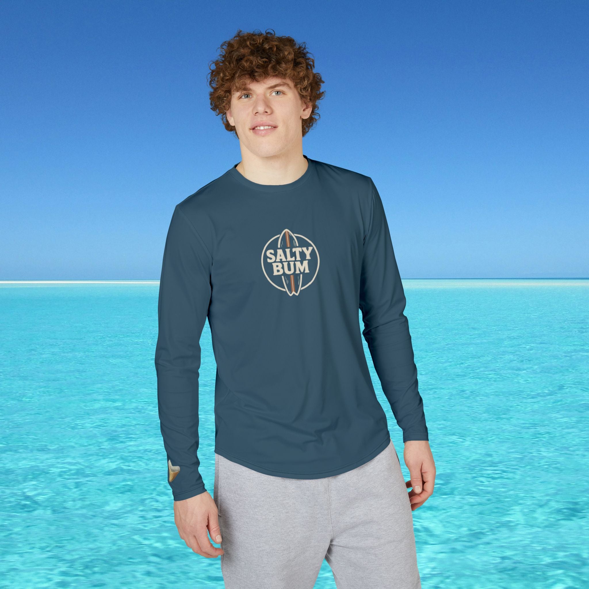 Person wearing a blue long-sleeve shirt with 'Salty Bum' logo against a clear blue sky and ocean background