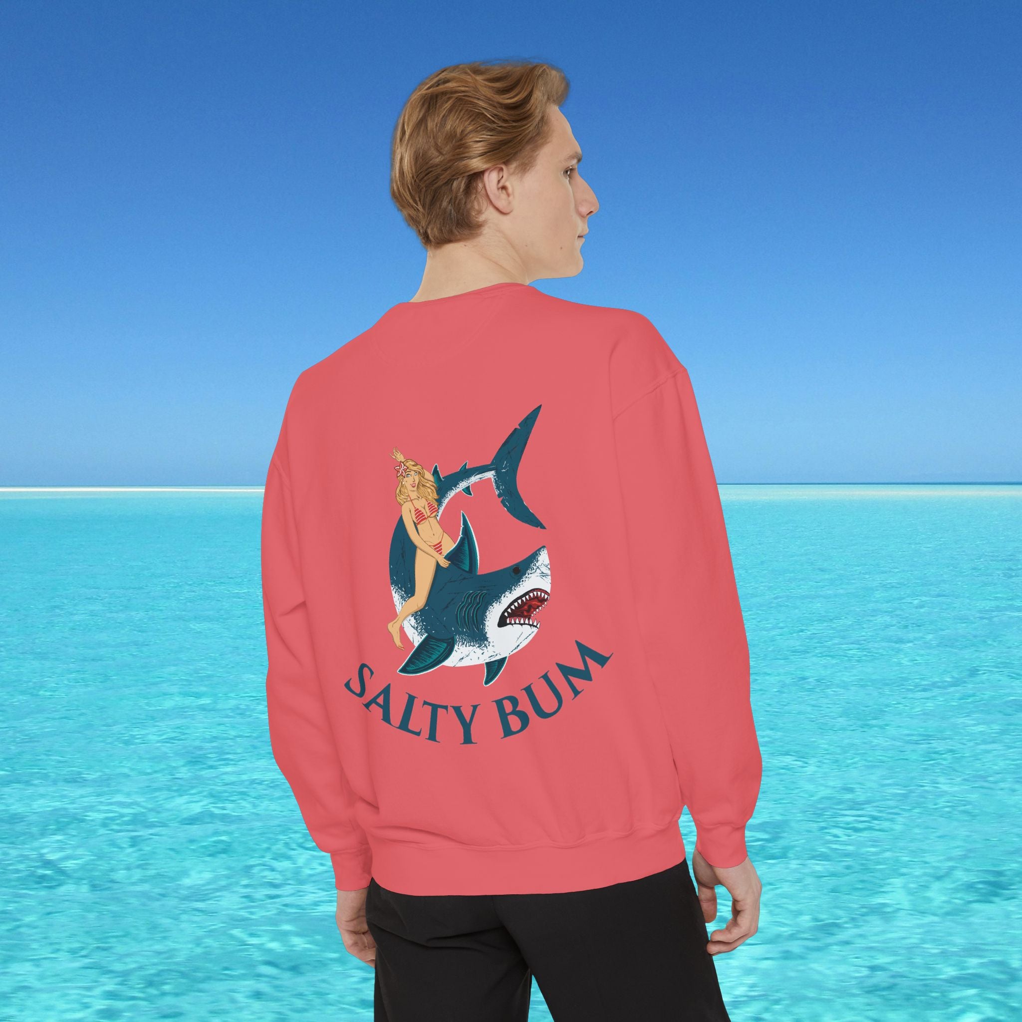 Person wearing a red sweatshirt with a shark and bikini graphic and 'Salty Bum' text, standing in front of a blue ocean.