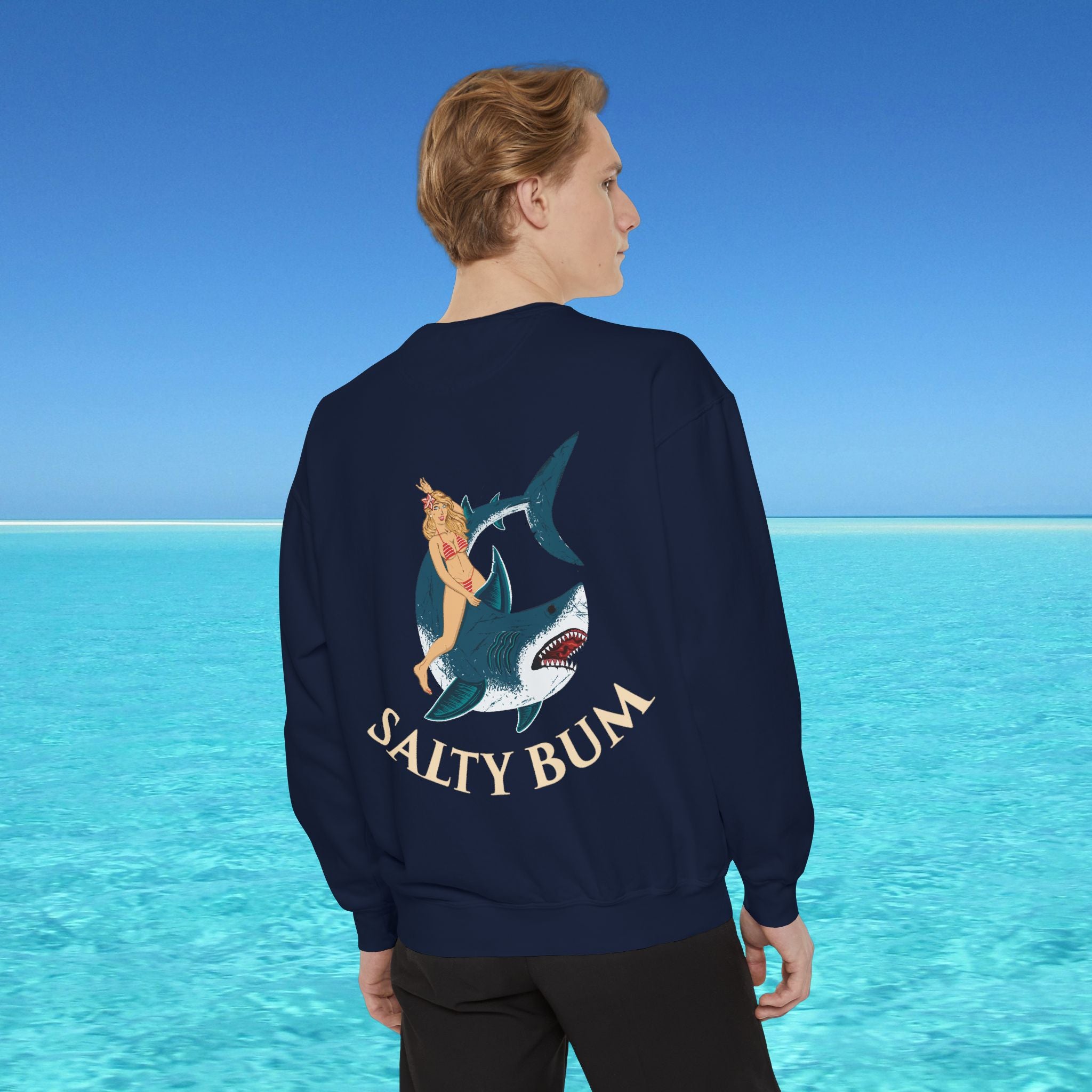 Person wearing a navy blue sweatshirt with a graphic design and text 'Salty Bum' against a clear blue sky and ocean background.
