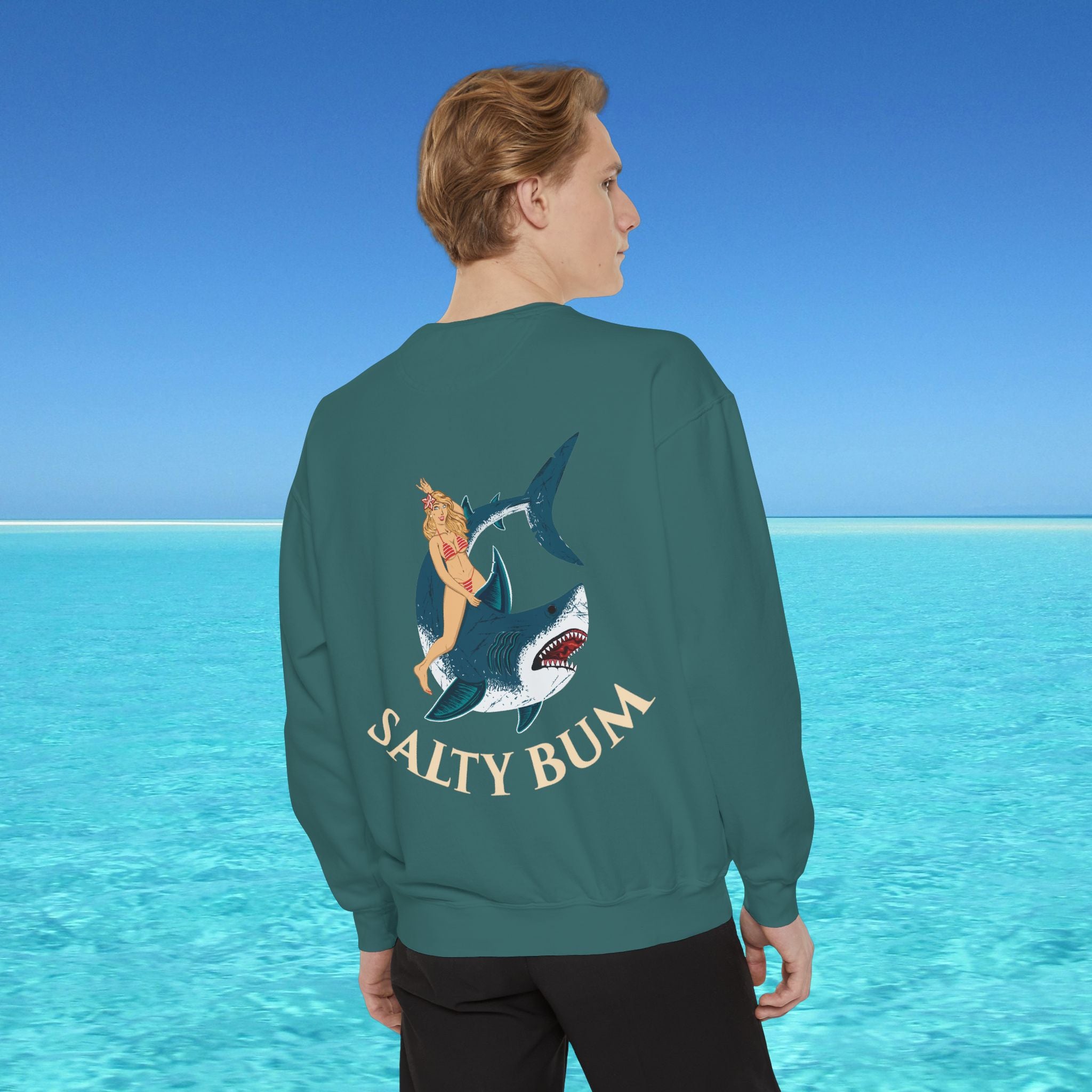 Person wearing a sweatshirt with a shark and bikini graphic and 'Salty Bum' text, standing in front of a blue ocean.