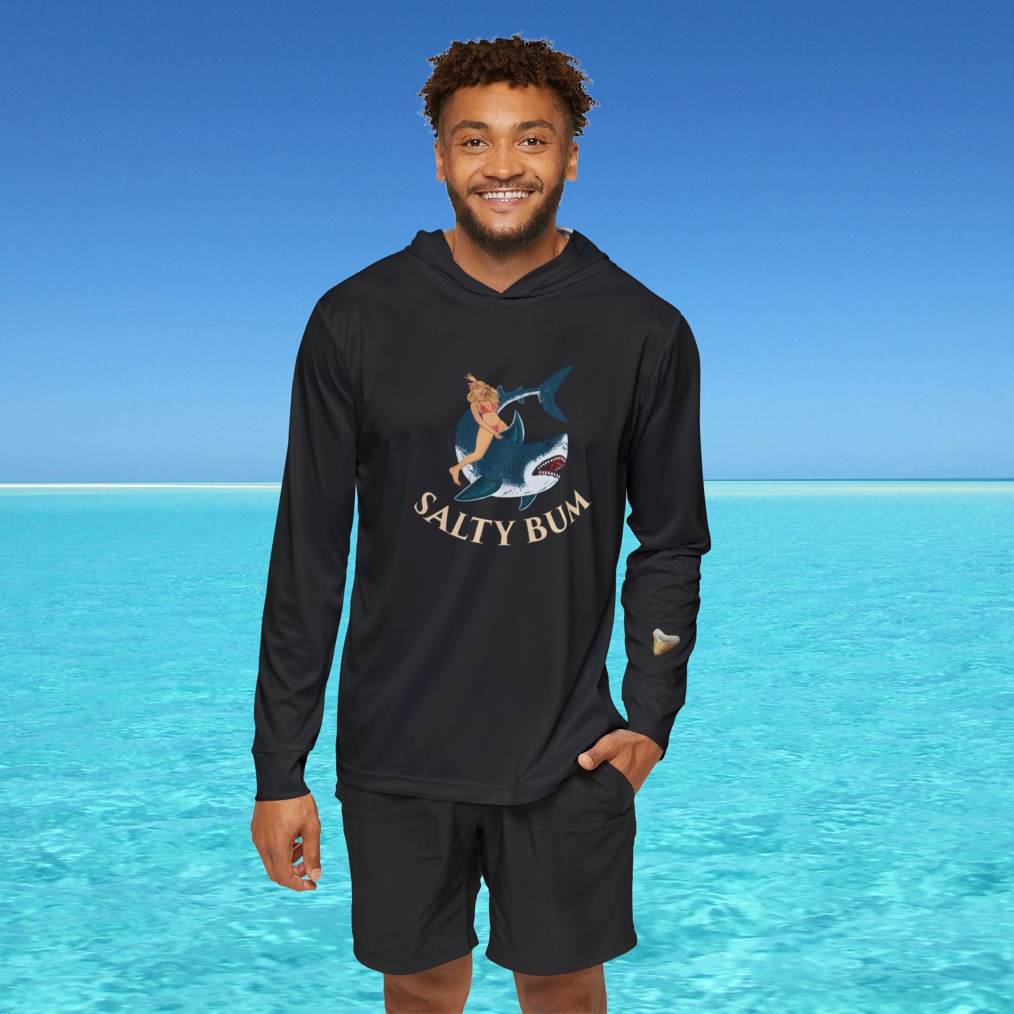 Man wearing a black long-sleeve shirt with 'Salty Bum' logo and shorts, standing in front of clear blue water.