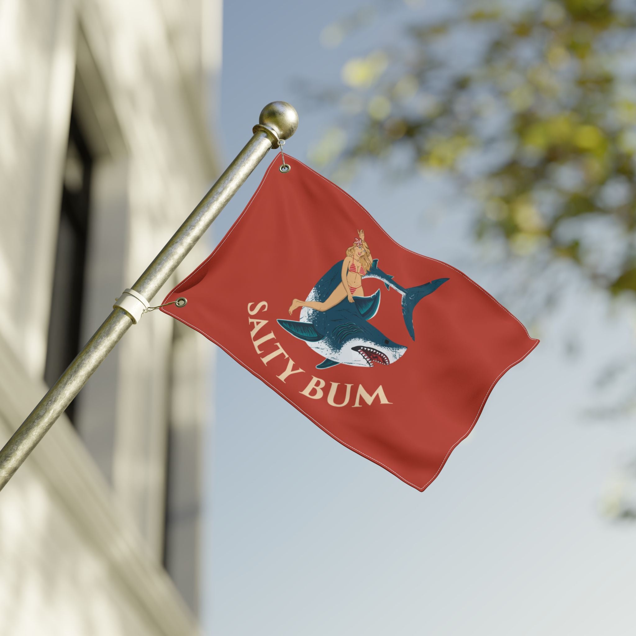 Red flag with 'Salty Bum' logo featuring a mermaid and shark, attached to a pole outdoors.