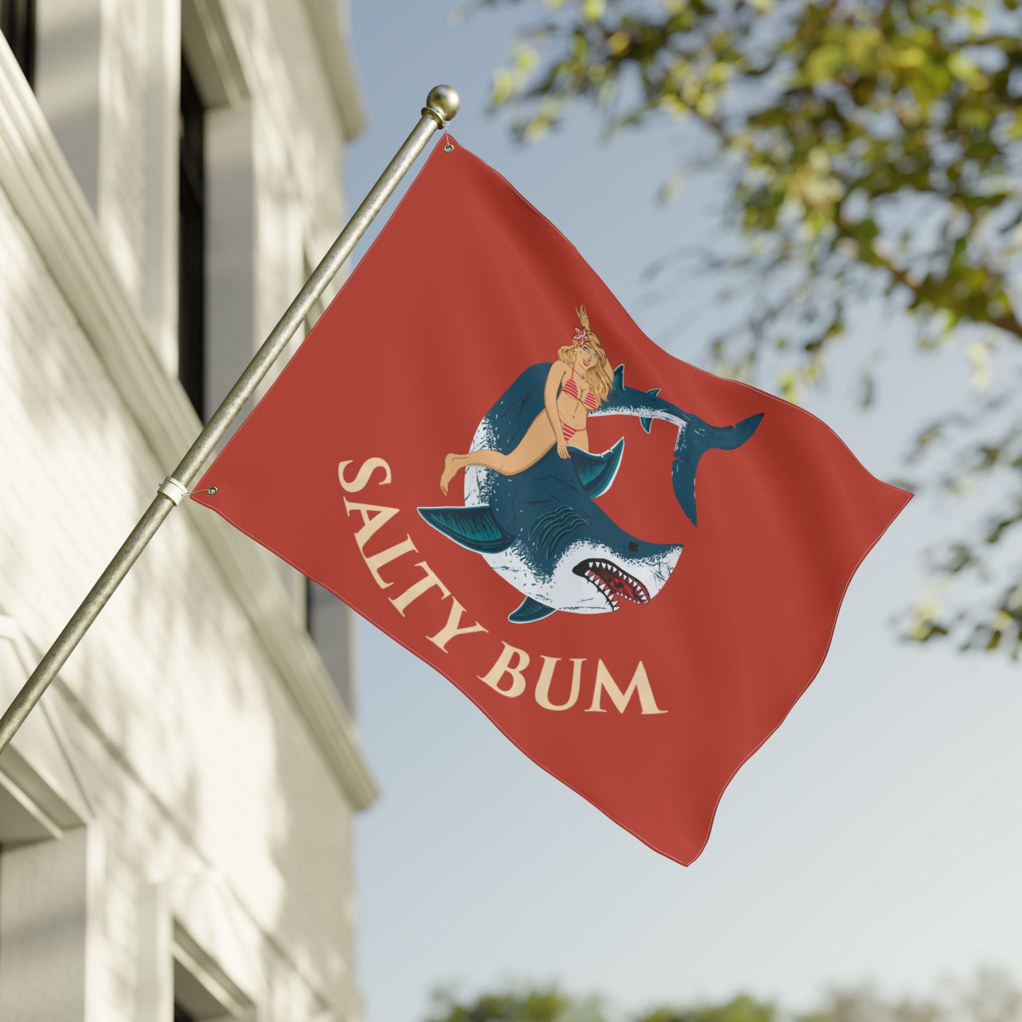 Red flag with a shark design and 'Salty Bum' text, waving in front of a building.