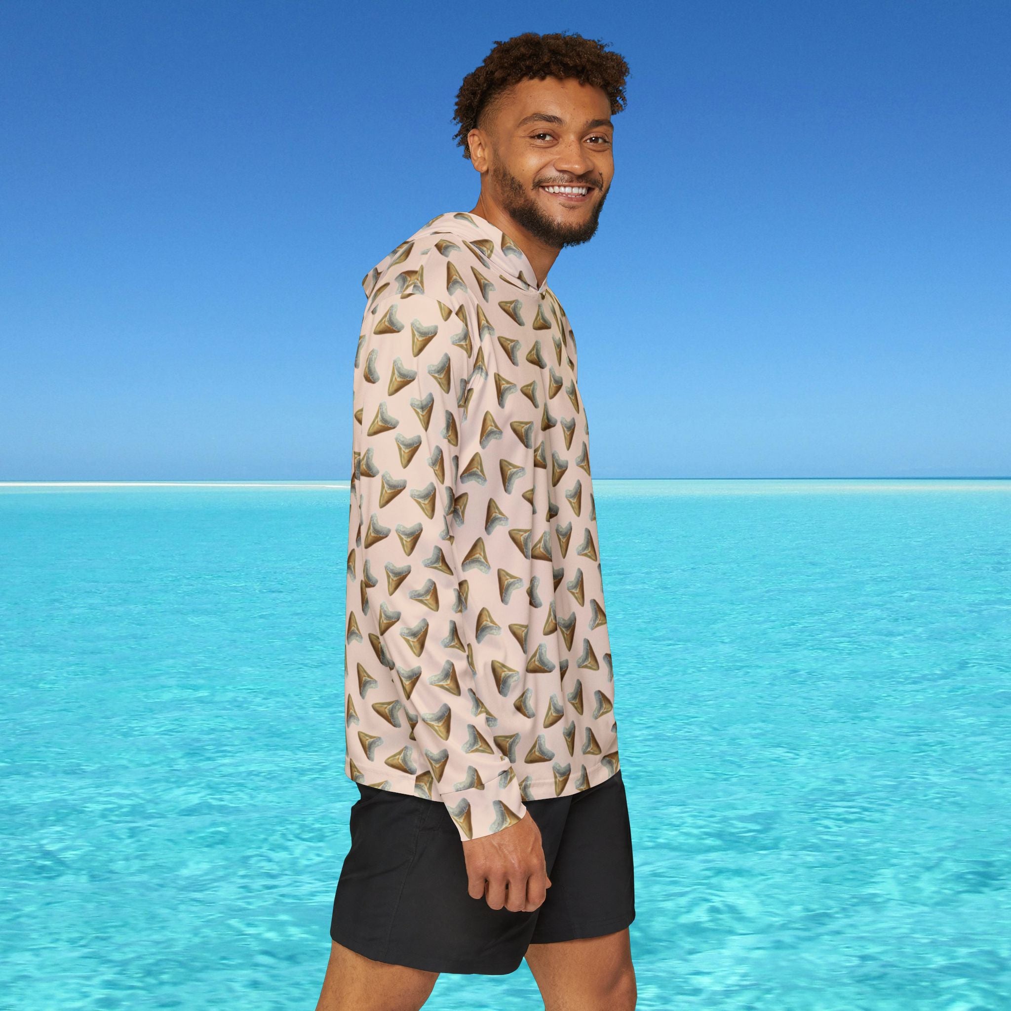 Man wearing a patterned shirt and black shorts standing in front of clear blue water and sky.