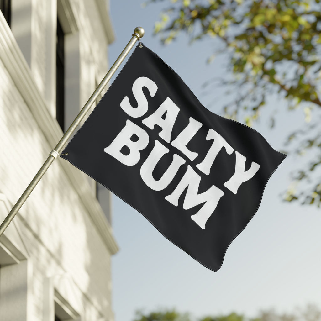 Black flag with 'Salty Bum' text waving in front of a building and tree.