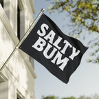 Black flag with 'Salty Bum' text waving in front of a building and tree.