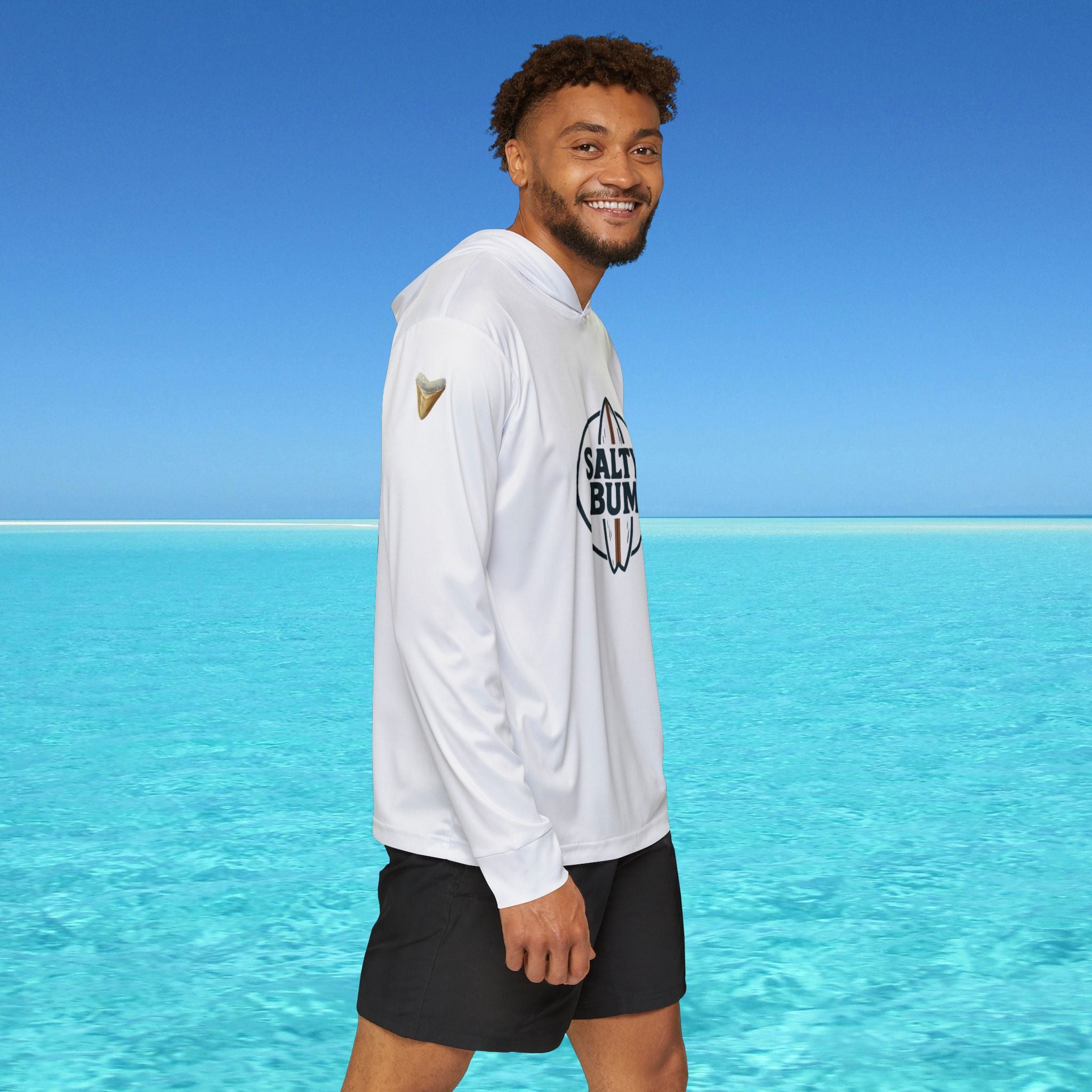 Man wearing a white hoodie with a logo and text, standing in front of clear blue water and sky.