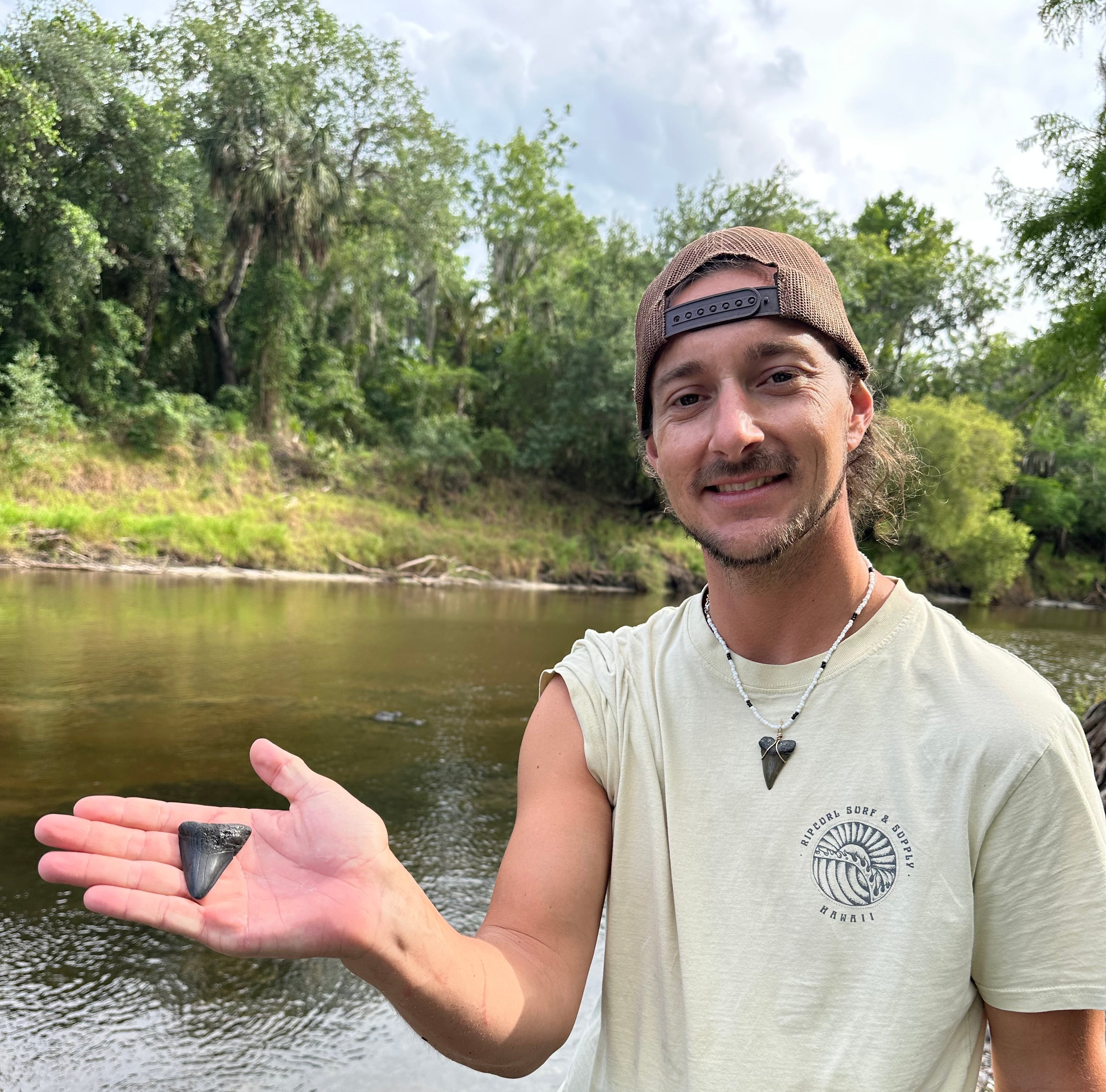 Person holding a turtle shell in front of a body of water with trees in the background